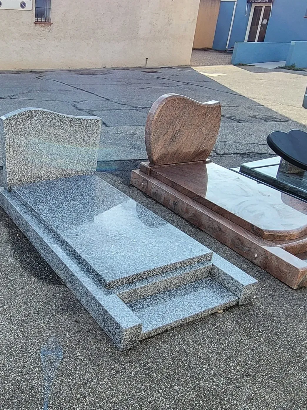 Exposition de monuments funéraires en granit gris et rose sur un site de marbrerie