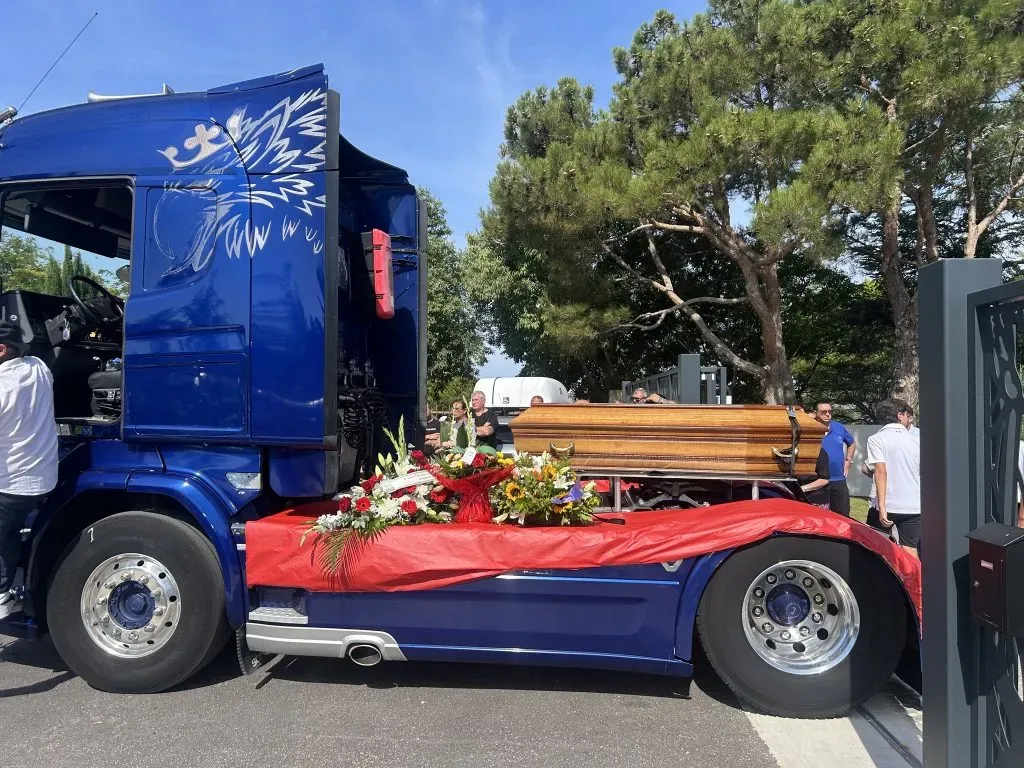 Camion poids lourd bleu transportant un cercueil en bois orné de fleurs pour un hommage personnalisé