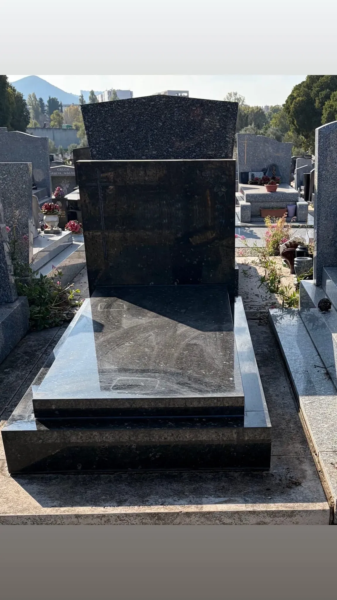 Tombe en granit noir poli avec stèle rectangulaire posée dans un cimetière