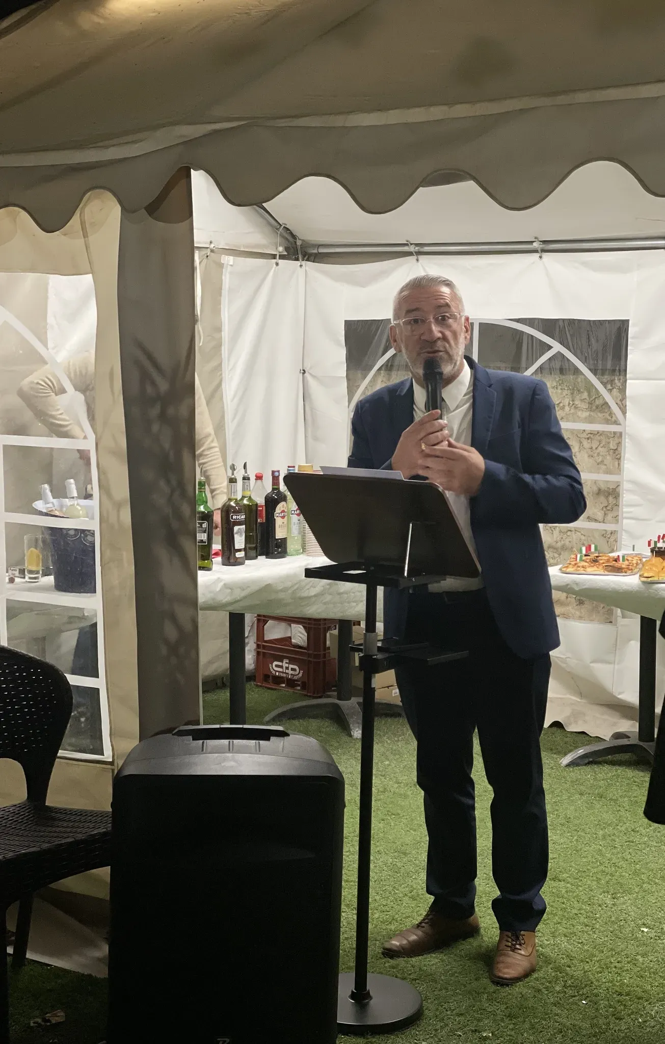 Homme en costume prononçant un discours au micro sous un chapiteau d'événement