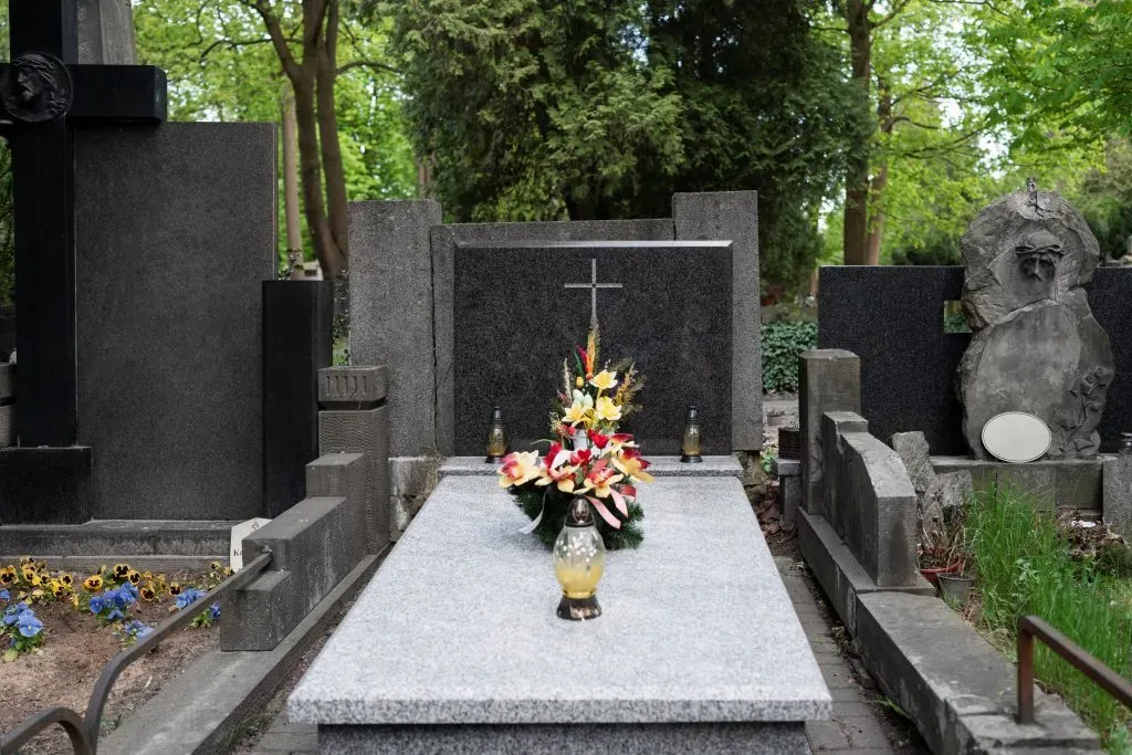 Monument funéraire en granit clair orné de fleurs et d'une croix chrétienne dans un cimetière arboré