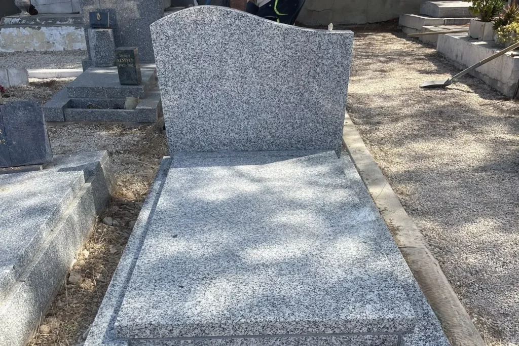 Monument funéraire individuel en granit gris moucheté avec stèle à sommet ondulé